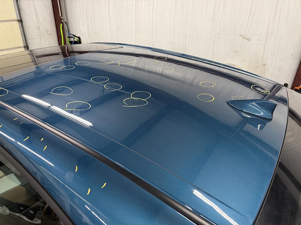 Roof of a sedan showing dozens of hail dents marked with chalk circles